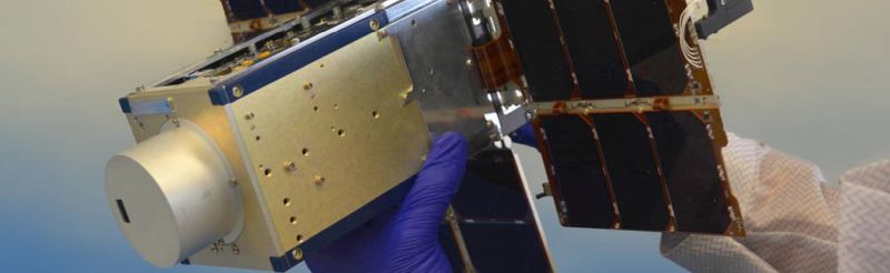 A researcher holds NACHOS fixed to a CubeSat with solar panels unfolded.