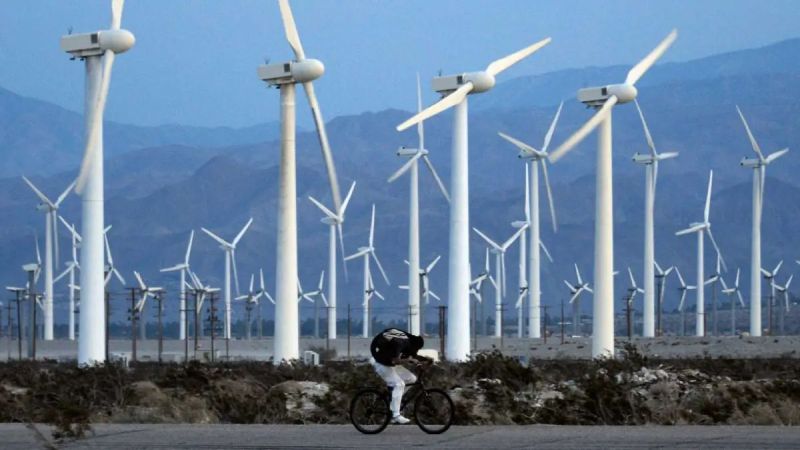 A man rides his bike against the wind as giant wind turbines are powered by strong winds at sunset on March 27, 2013, in Palm Springs, California.